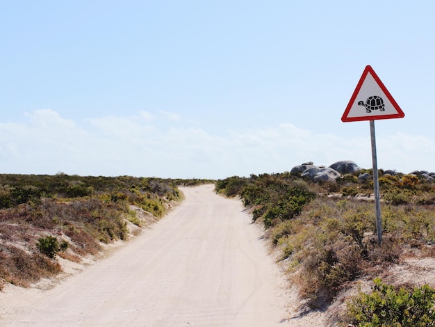 animal crossing sign by dirt road against sky