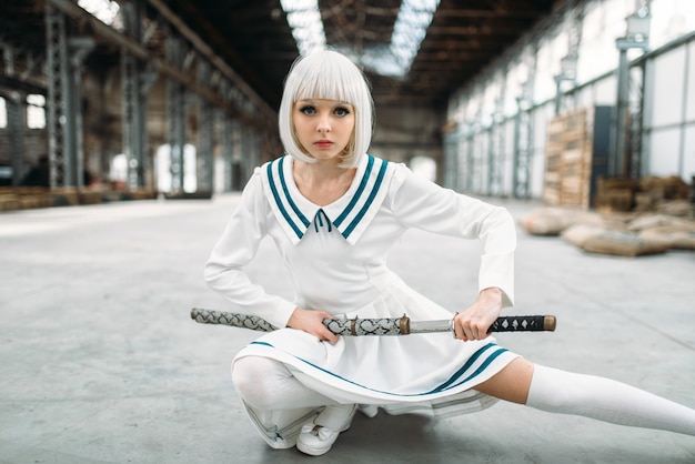 Anime-stijl blonde vrouw met zwaard. Cosplay mode, japanse cultuur, pop met mes op verlaten fabriek