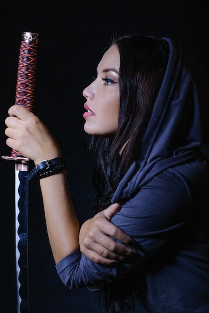 Стилизованная в стиле аниме брюнетка с длинными волосами, суровым взглядом смотрящая на нее с мечом катана