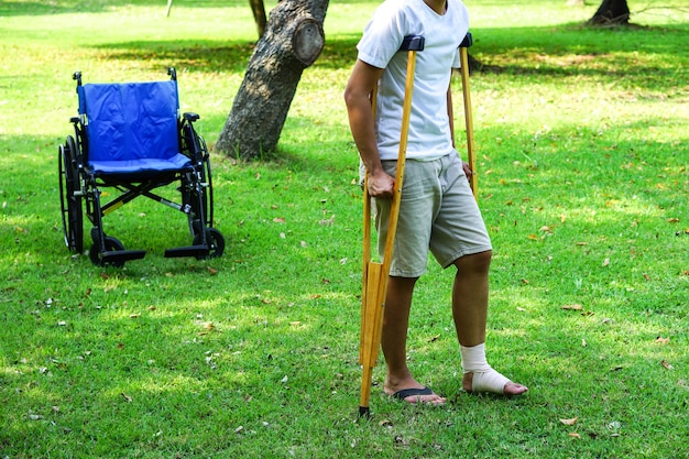 발목 부상 환자는 뒤에 휠체어가 있는 잔디밭에서 목발을 사용하여 지지합니다.