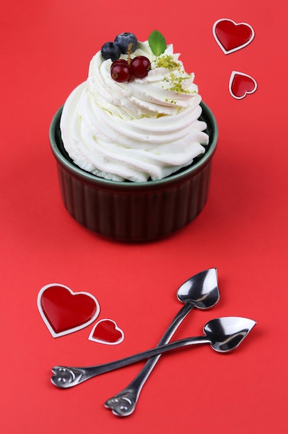 Фото Белковый десерт анны павловой на красном фоне с ложками в форме сердца и красными сердцами рядом, декор