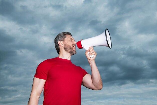 Announcer in red shirt shout in loudspeaker on sky background