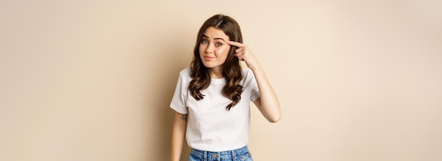 Annoyed and angry woman pointing finger at head scolding\
someone standing over beige background