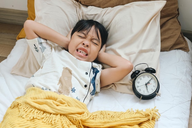 Photo annoyed boy being awakened by an alarm clock in bedroom on morning