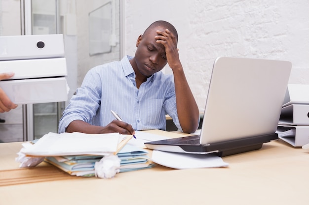 Annoyed businessman taking notes while holding his head