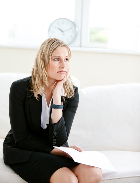 Photo annoyed businesswoman holding a paper and sitting on a sofa