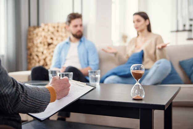 Annoyed caucasian couple of man and woman having conversation with psychologist on therapy session in light room.