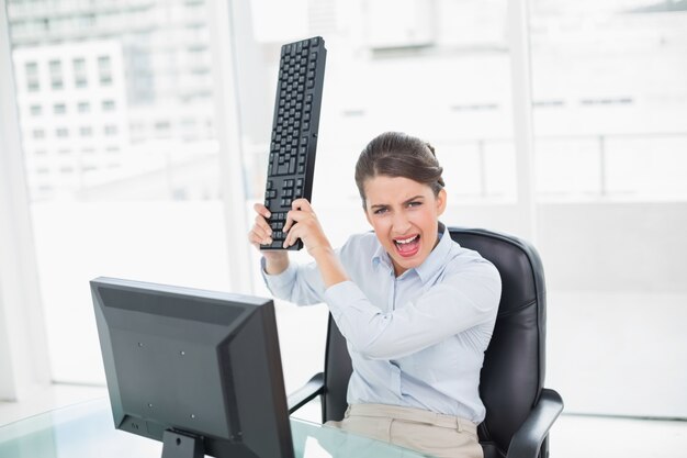 彼女のコンピュータに彼女のキーボードを投げている迷惑な茶色の髪の実業家