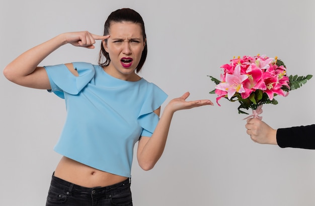 Annoyed pretty young woman pointing at someone giving bouquet of flowers to her