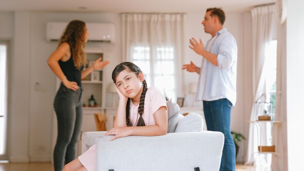 Photo annoyed and unhappy young girl sitting on sofa trapped in middle of tension by her parent argument in living room unhealthy domestic lifestyle and traumatic childhood develop to depression synchronos