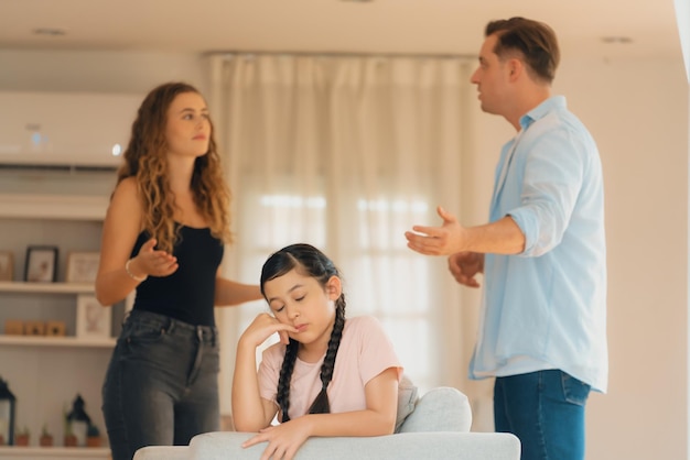 annoyed and unhappy young girl sitting on sofa trapped in middle of tension by her parent argument in living room unhealthy domestic lifestyle and traumatic childhood develop to depressionsynchronos