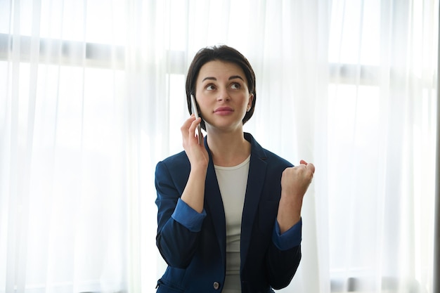 Раздраженная женщина, бизнесвумен, офисный работник сжимает кулак и гневно смотрит вверх во время скучного утомительного телефонного разговора с собеседником