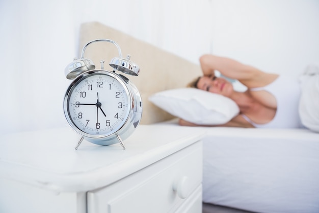 Annoyed woman covering her ears from alarm clock noise in bed