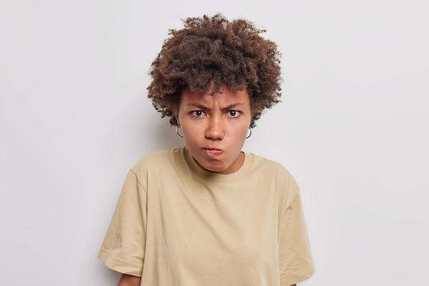 Annoyed woman smirks face looks angrily at camera feels irritated purses lips wears casual basic t shirt isolated on white background Frustrated pretty female model feels outraged Negative emotions