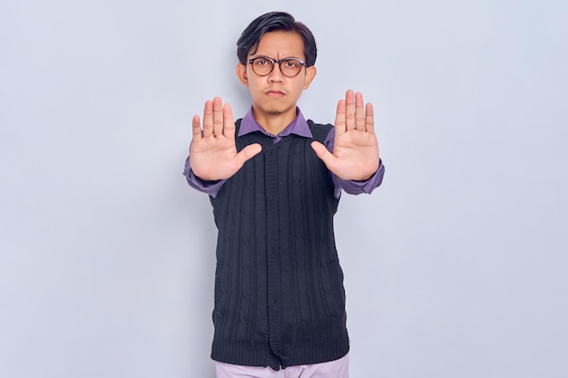 Annoyed young asian man in casual shirt makes stop gesture
saying no isolated on white background