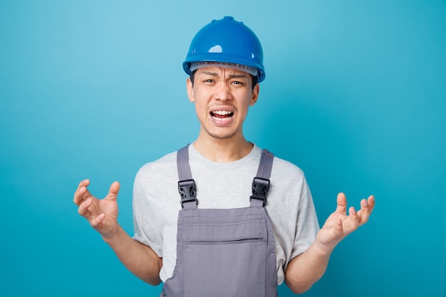 Annoyed young construction worker wearing safety helmet and uniform doing tiger paws gesture 