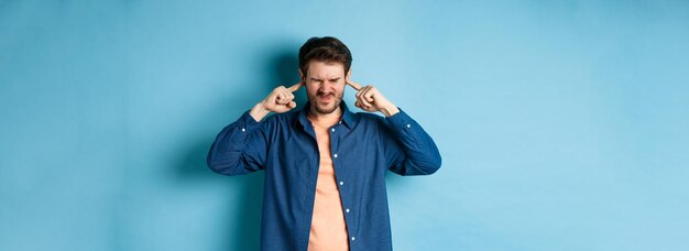 annoyed young man block sound shut ears with fingers and grimacing disturbed by loud music standing