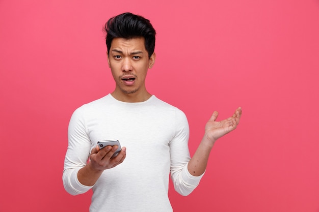 Annoyed young man holding mobile phone showing empty hand 