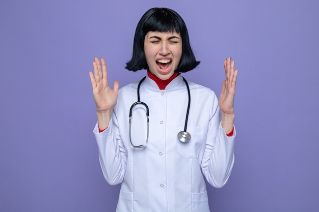 Annoyed young pretty caucasian girl in doctor uniform with stethoscope stands with closed eyes holding hands open