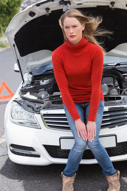 Annoyed young woman beside her broken down car