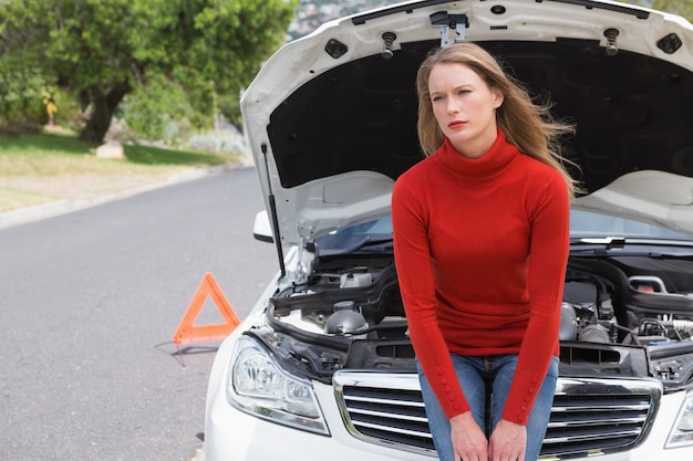 Annoyed young woman beside her broken down car