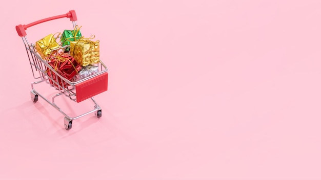 Annual sale Christmas shopping season concept mini red shop cart trolley full of gift box isolated on pale pink background copy space close up