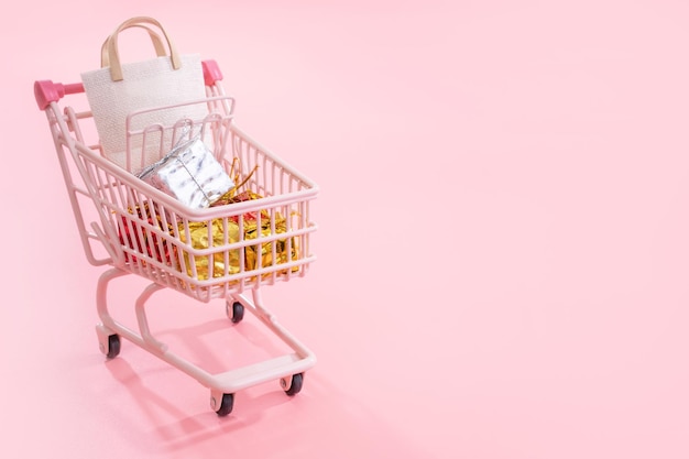 Annual sale shopping season concept mini pink shop cart trolley full of paper bag gift isolated on pale pink background blank copy space close up