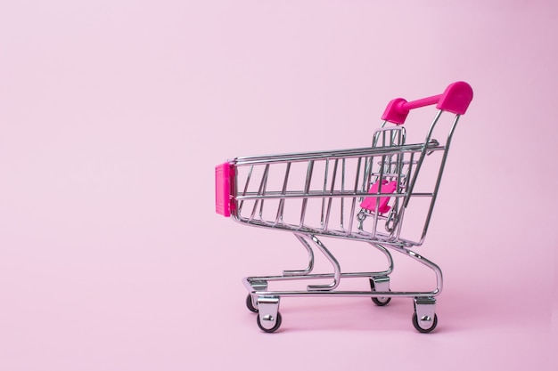 Annual sale shopping season concept - mini pink shop cart trolley on pale pink background,