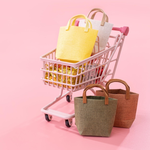 Annual sale shopping season concept mini red shop cart trolley full of paper bag gift isolated on pale pink background blank copy space close up