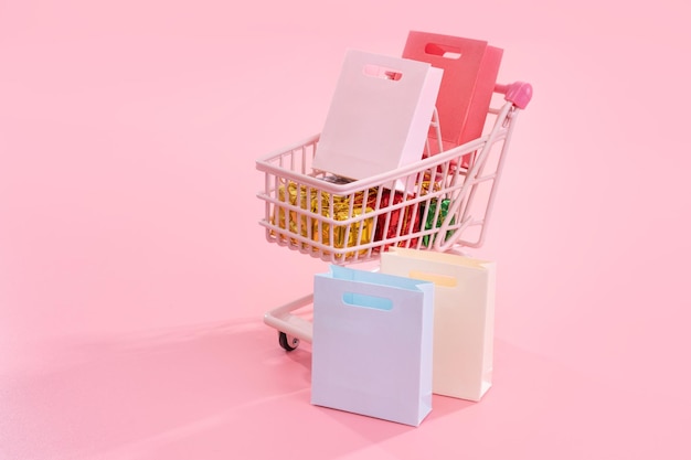 Annual sale shopping season concept mini red shop cart trolley full of paper bag gift isolated on pale pink background blank copy space close up