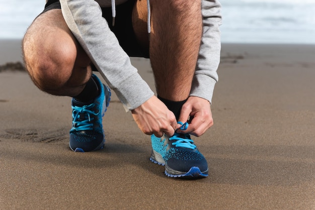 Anonieme close-up van man die sportschoenen bindt op het strand