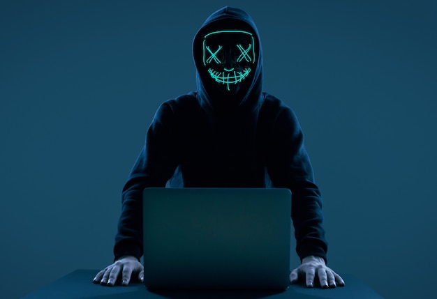 Anonieme man in een zwarte hoodie en neon masker hacken van een computer