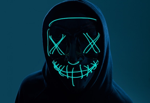 Anonieme man in zwarte hoodie die zijn gezicht verbergt achter een neonmasker
