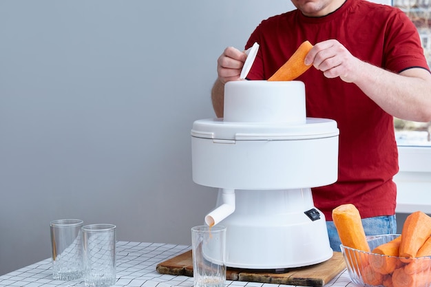 Anonieme man zet wortelen in een industriële juicer. Ruimte kopiëren.