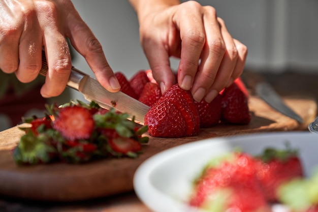 Anonieme persoon bijsnijden die verse aardbeien op een houten bord snijdt terwijl hij een gezond gerecht bereidt