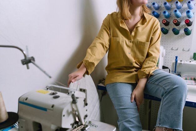 Anonieme schot van jonge vrouw in geel overhemd zit in haar naaiatelier voor de kleurrijke draden