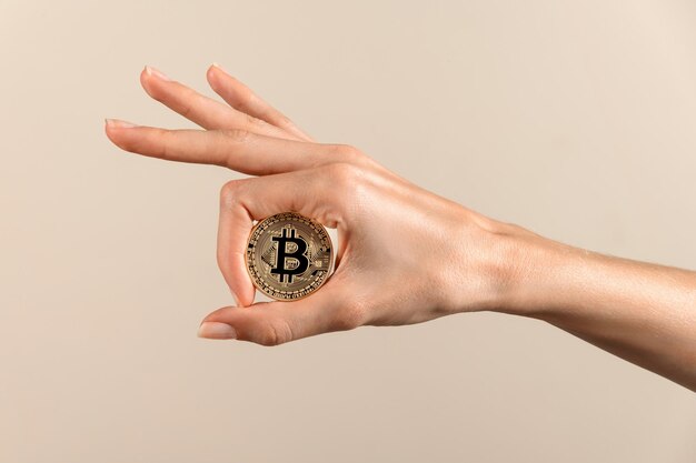 Anonieme vrouw met ronde bitcoin met B in het midden met gemanipuleerde duim en wijsvinger van de hand die licht weerkaatst op een beige achtergrond
