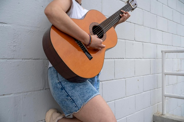 Anonieme vrouwelijke gitarist met regenboog armband die muziek speelt op akoestische gitaar terwijl ze naast een metalen hek op straat op een openbare plaats staat