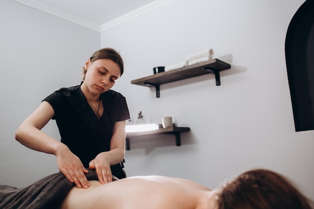 Anonymous female masseur pressing on back of client with elbows while doing traditional massage in light modern clinic