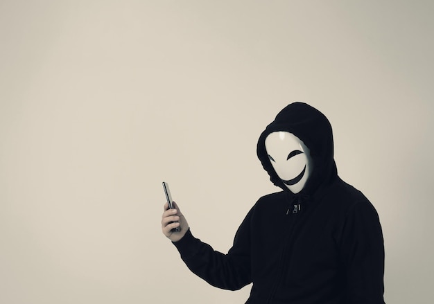 Anonymous hacker and face mask with smartphone in hand