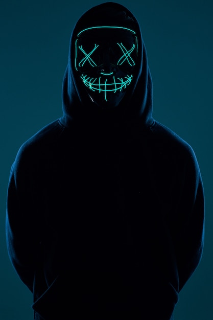 Anonymous man in black hoodie hiding his face behind a neon mask