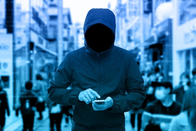 Anonymous man in a black hoodie using smartphone hacking