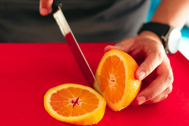Photo anonymous man cutting an orange at home. close-up photo