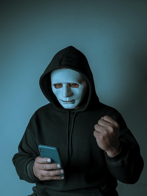 An anonymous masked hacker is using a smartphone to penetrate credit card financial information Hacking and malware concept