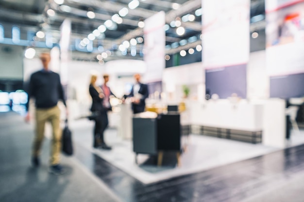 Photo anonymous people standing and walking on a trade show booth, generic background with a blur effect applied