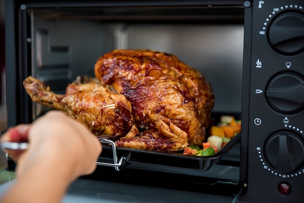 Anonymous person taking grilled chicken from oven