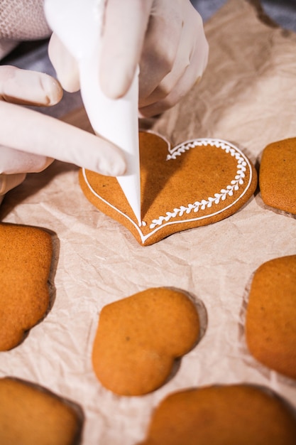Anonymous woman decorating some homemade heart gingerbread cookies at kitchen