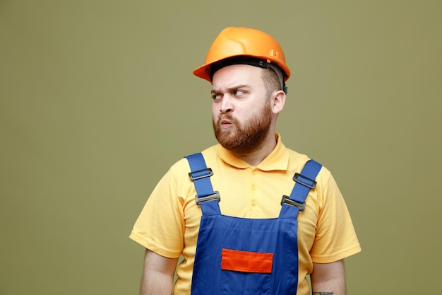 Anpleased looking at side young builder man in uniform isolated on green background