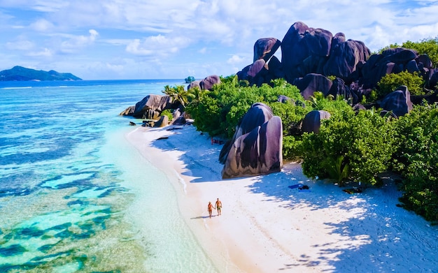 セイシェル諸島のラ・ディグー (La Digue) のドローン飛行写真 (Drone aerial view of La Digue Seychelles) は豪華な休暇で日没中にビーチで歩いているカップル男性と女性の鳥眼写真です