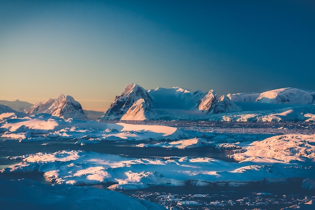 Antarctic landscape with snow covered mountains against blue sky sunset warm light on the mountain